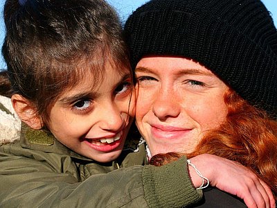 Eine junge Frau hält ein Mädchen im Arm, beide lächeln in die Kamera