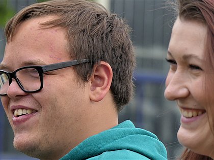 Ein junger Bewohner und eine Mitarbeiterin blicken lächelnd in eine Richtung