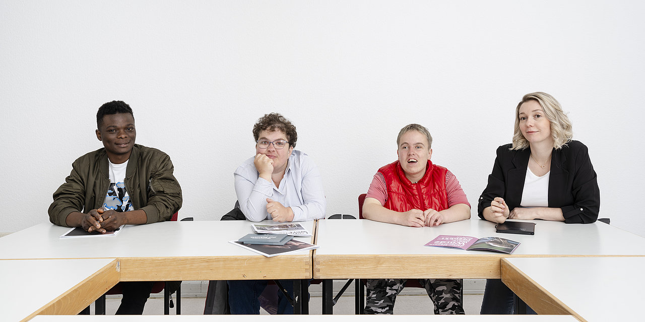 Vier Menschen sitzen an einem Tisch und blicken in die Kamera
