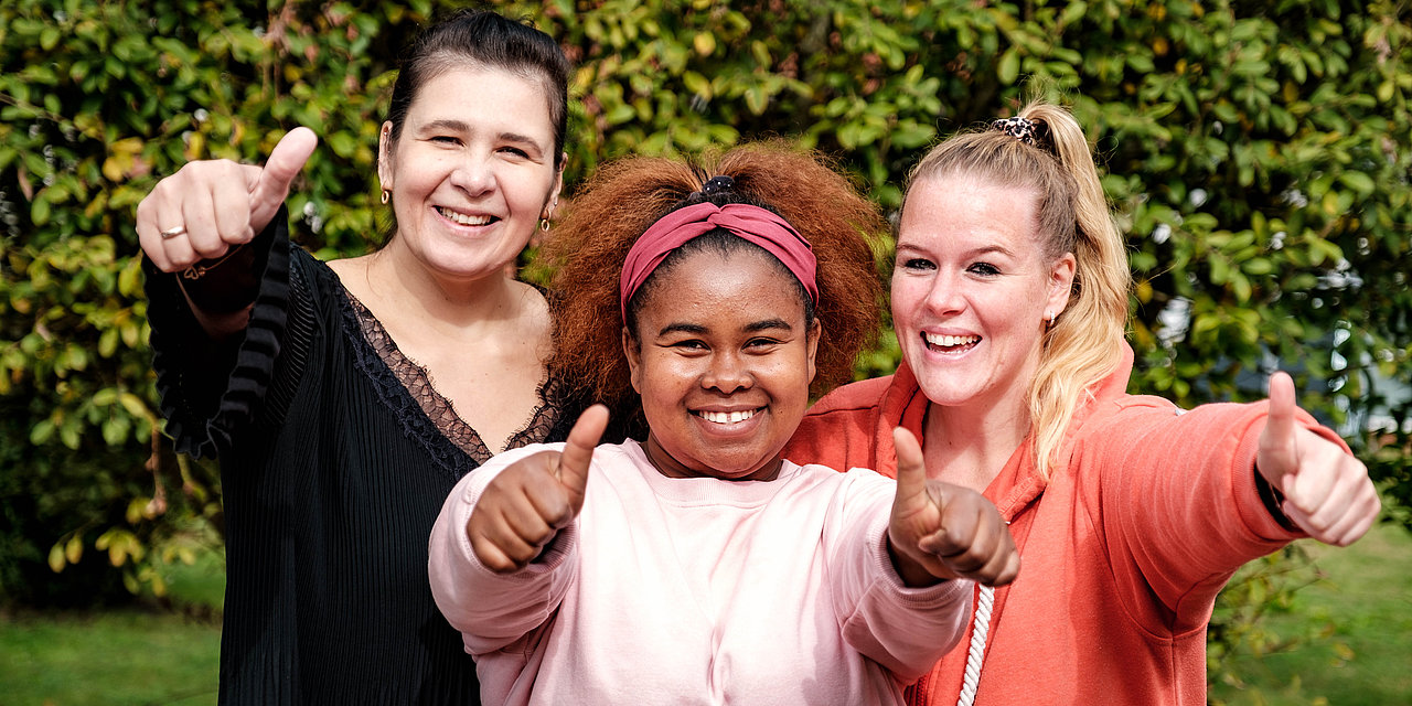 Drei junge Frauen haben den Daumen gehoben und lächeln in die Kamera