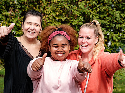 Drei junge Frauen haben den Daumen gehoben und lächeln in die Kamera