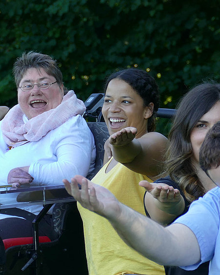 Eine Gruppe junger, gut gelaunter Menschen sitzt im Freien nebeneinander 