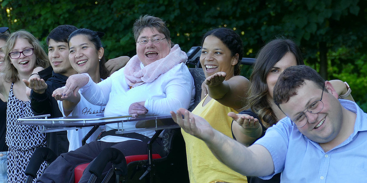 Eine Gruppe junger, gut gelaunter Menschen sitzt im Freien nebeneinander 