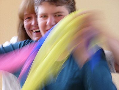 Eine junge Frau schwenkt bunte Tücher, eine andere steht hinter ihr, beide lächeln in die Kamera