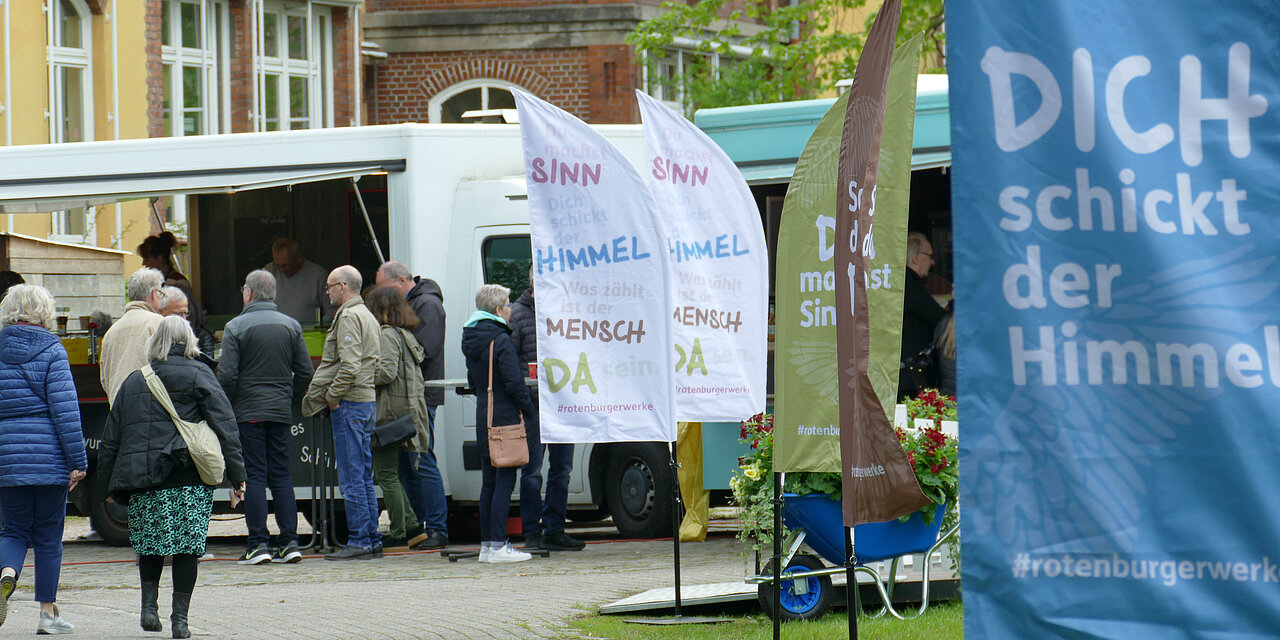 Junge Leute stehen auf einer Wiese in Gruppen zusammen, Fahnen mit Dich schickt der Himmel und anderen Slogans sind zu lesen