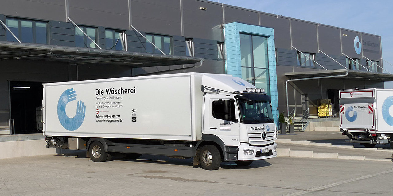 Ein weißer Lastwagen mit blauem Logo steht vor der Wäscherei der Rotenburger Werke