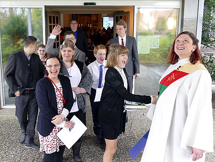 Junge, festlich gekleidete Menschen verlassen strahlend mit ihrer Diakonin die Kirche