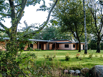 Ein modernes Holzhaus mit Flachdach im Grünen unter Bäumen