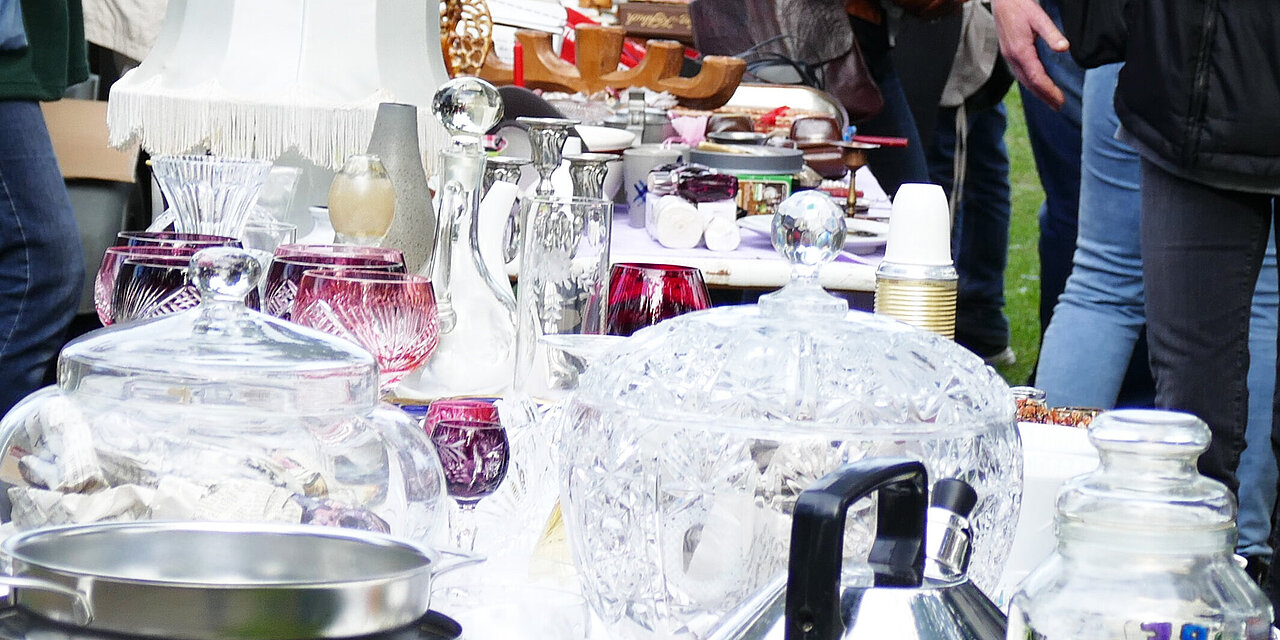Ein langer Tisch mit Geschirr und Trödel, an dem Menschen vorübergehen 